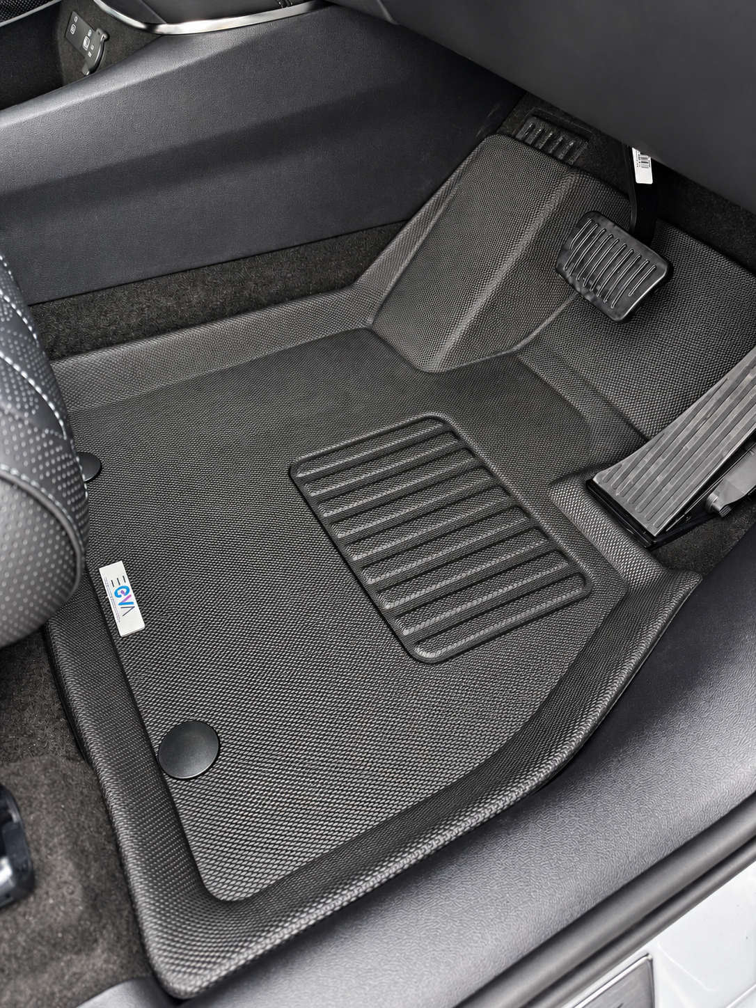 EEVA-branded XPE floor mat fitted in a driver's footwell, showing the logo label, textured surface and raised edges.
